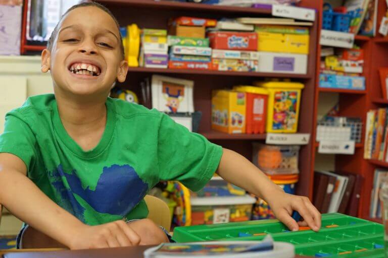 Student in green shirt smiling while playing with educational game